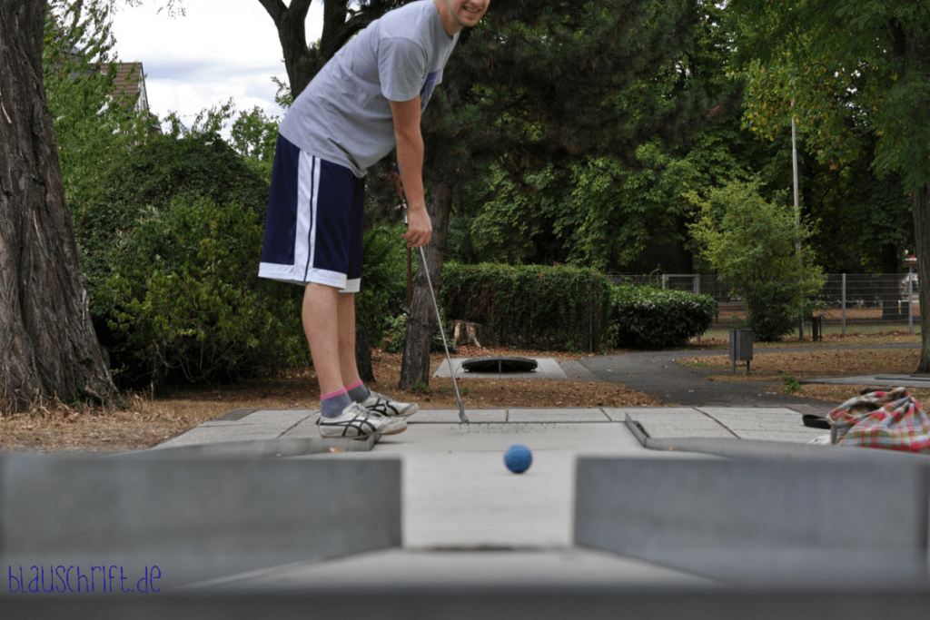 Spieler verfolgt angespannt den Ball auf der Minigolfbahn