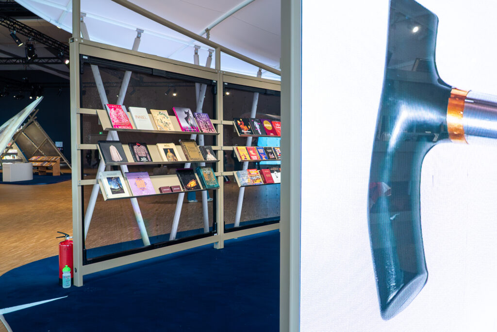 Im Vordergrund ein großer Screen, im Hintergrund Bücher in einem aufwendigen Messestand.