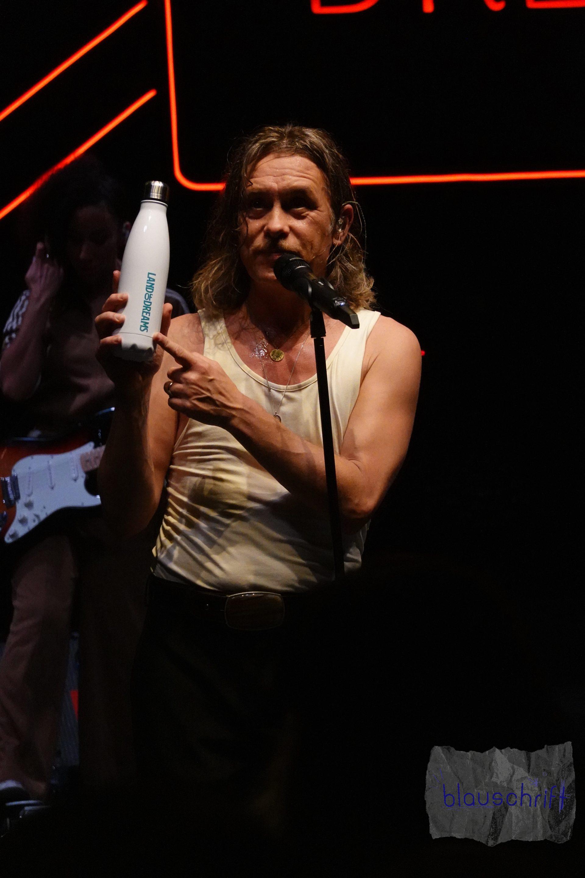 Mark Owen zeigt seine "Land of Dreams"-Flasche auf der Bühne