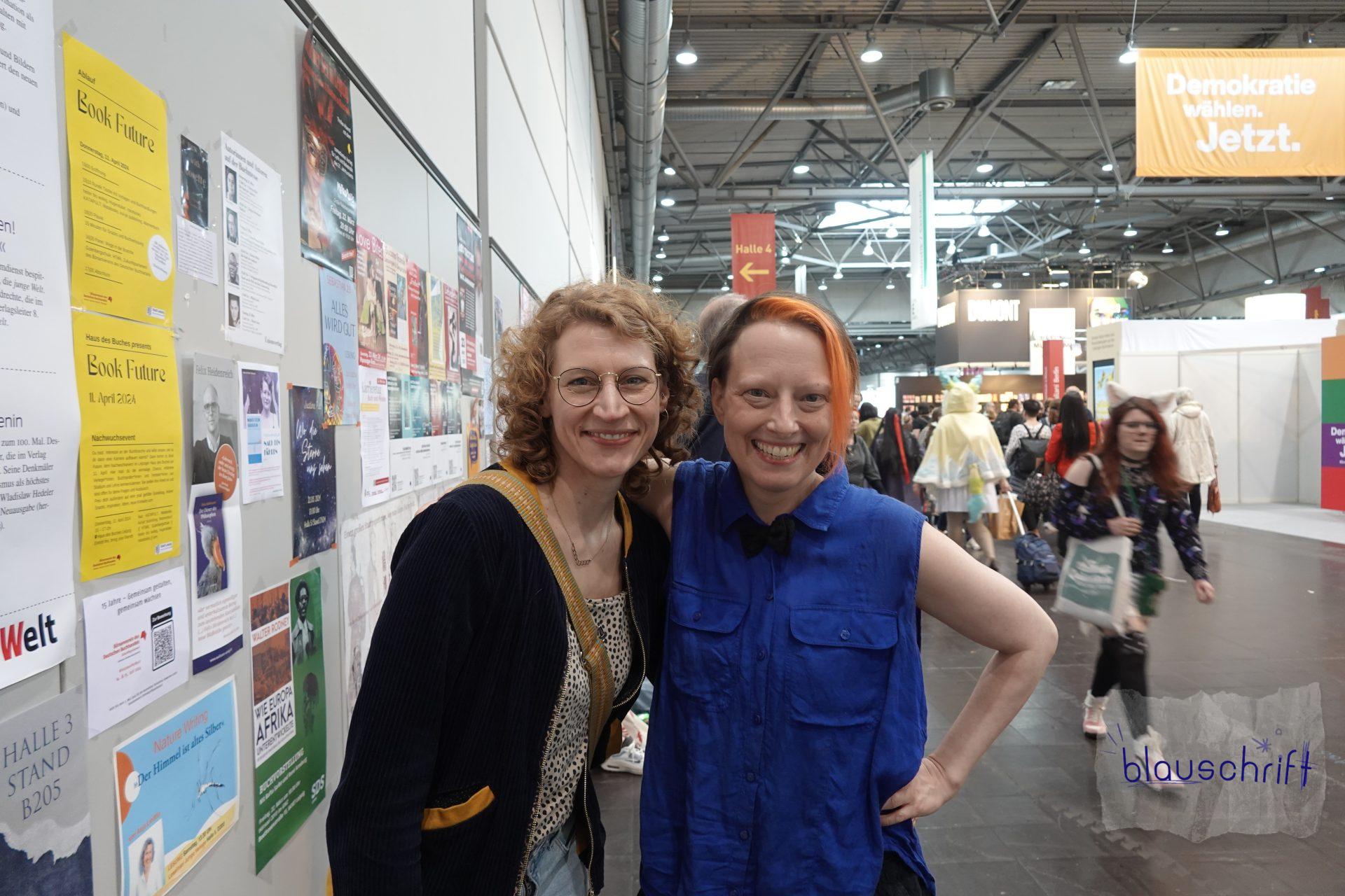 Stefanie und Alex stehen zusammen im Messegang der Halle 3 und lachen in die Kamera