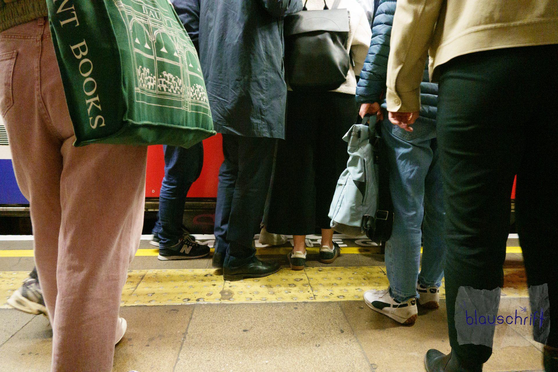 Viele Menschen drängen sich an die Tür einer Tube in London. Sie sind von den Füßen bis zur Körpermitte von hinten fotografiert.