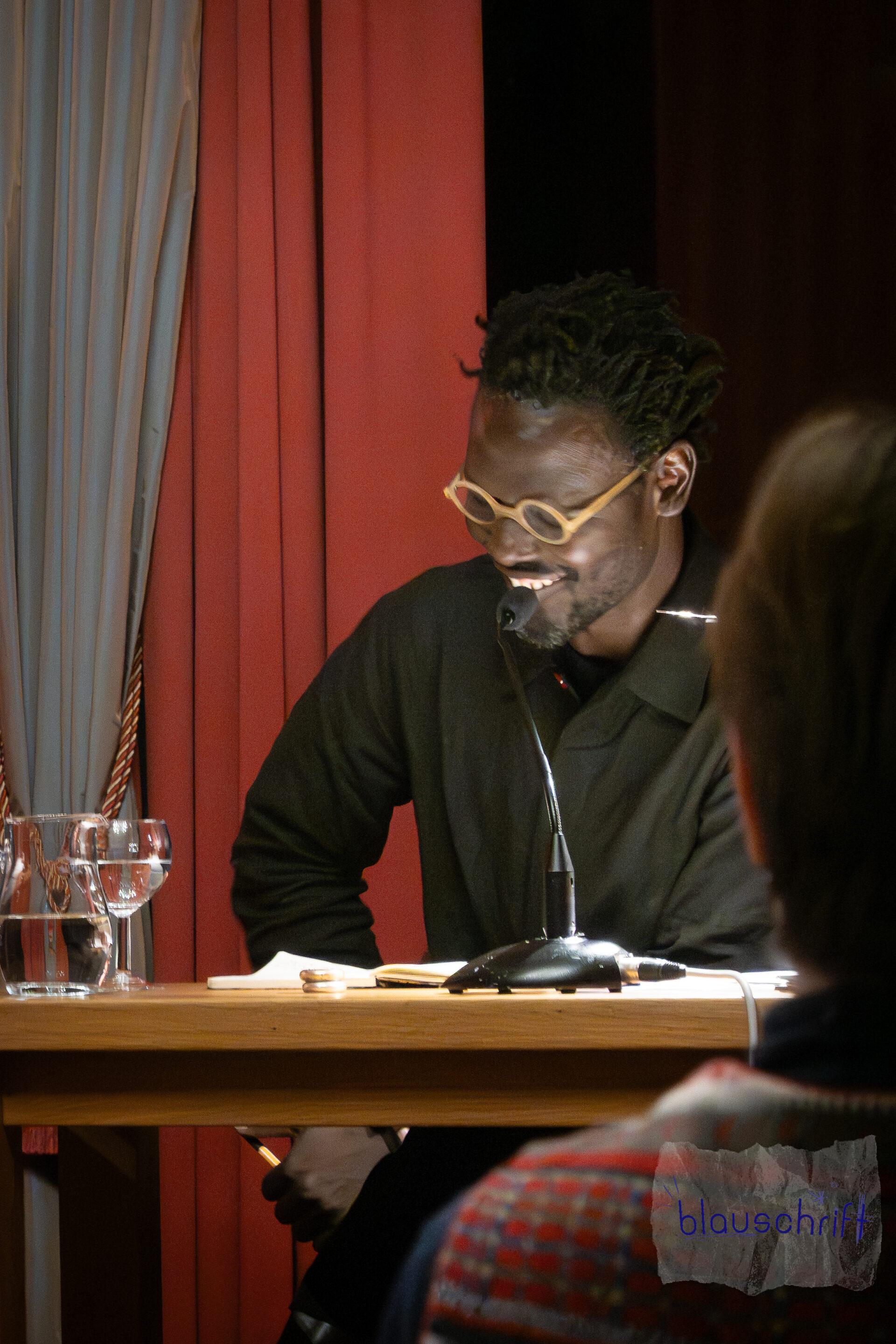 Moderator Ibou C. Diop sitzt lächelnd vor dem Mikro.